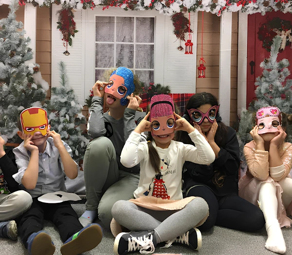 Дети сидят в комнате, украшенной к Рождеству. Дети в ярких масках кукол, супергероев и популярных персонажей, они улыбаются, проводят бал-маскарад. Праздничное настроение