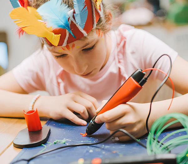 Подросток в шуточной короне сидя за столом делает рисунок с помощью специального карандаша.