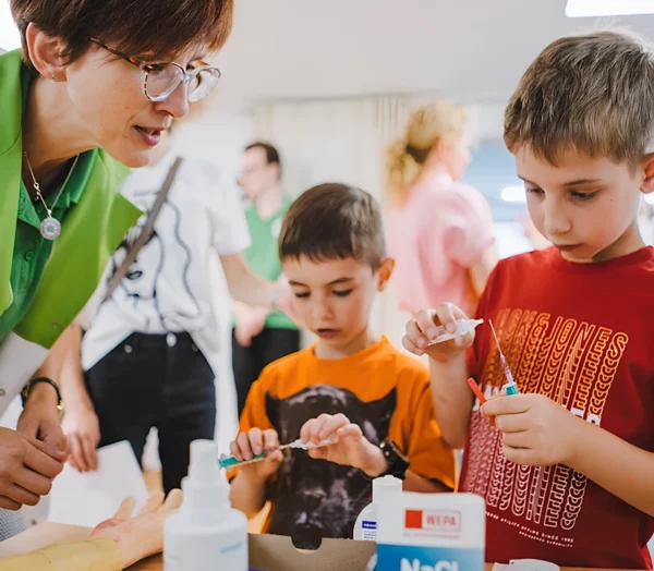 Подростки наполняют шприцы лекарством. Педагог курирует процесс.